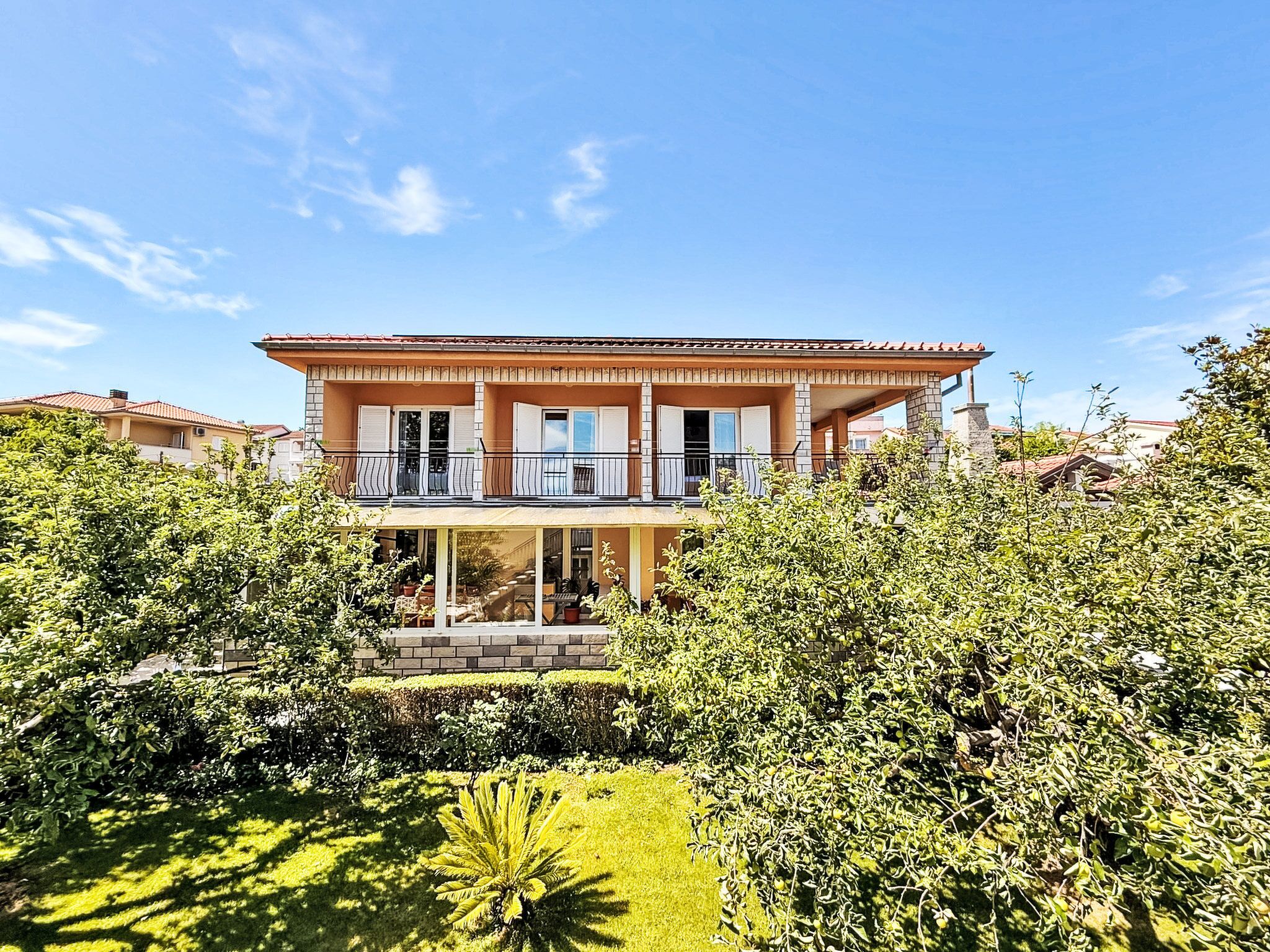 A two-story house with a balcony, surrounded by greenery.