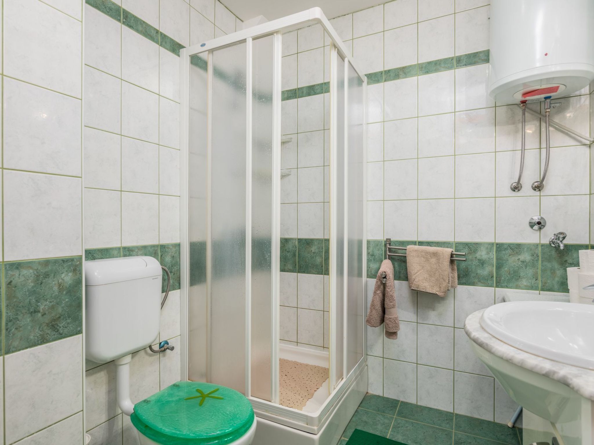 Une salle de bain comprenant un espace douche, des toilettes, un lavabo et un porte-serviettes.