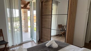 Une chambre d’hôtel avec un lit, une armoire en bois, une chaise et une vue sur l’extérieur grâce à une porte vitrée.