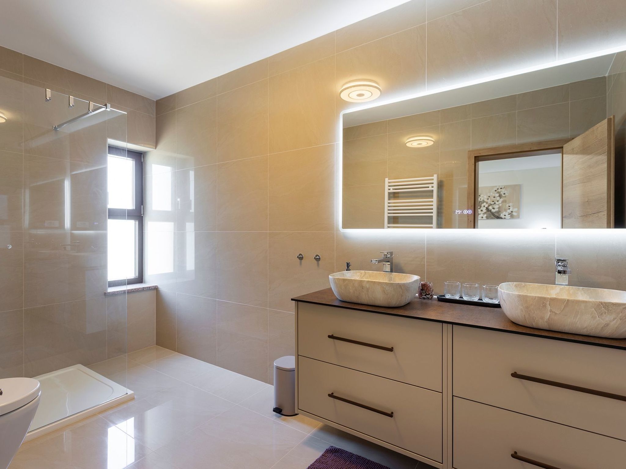 A modern bathroom with a large mirror, two sinks, and a toilet.