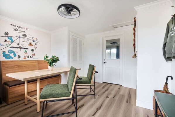 Una habitación moderna con una mesa de comedor de madera, dos sillas tapizadas de color verde, una pequeña planta en maceta y un mapa mural.
