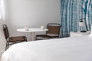 A hotel room with a bed, a round table with two chairs, a nightstand with a lamp, and a window with curtains.