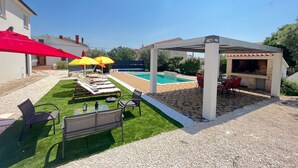 Ein Garten mit Pool, Sitzgelegenheiten im Freien und einer Grillanlage.