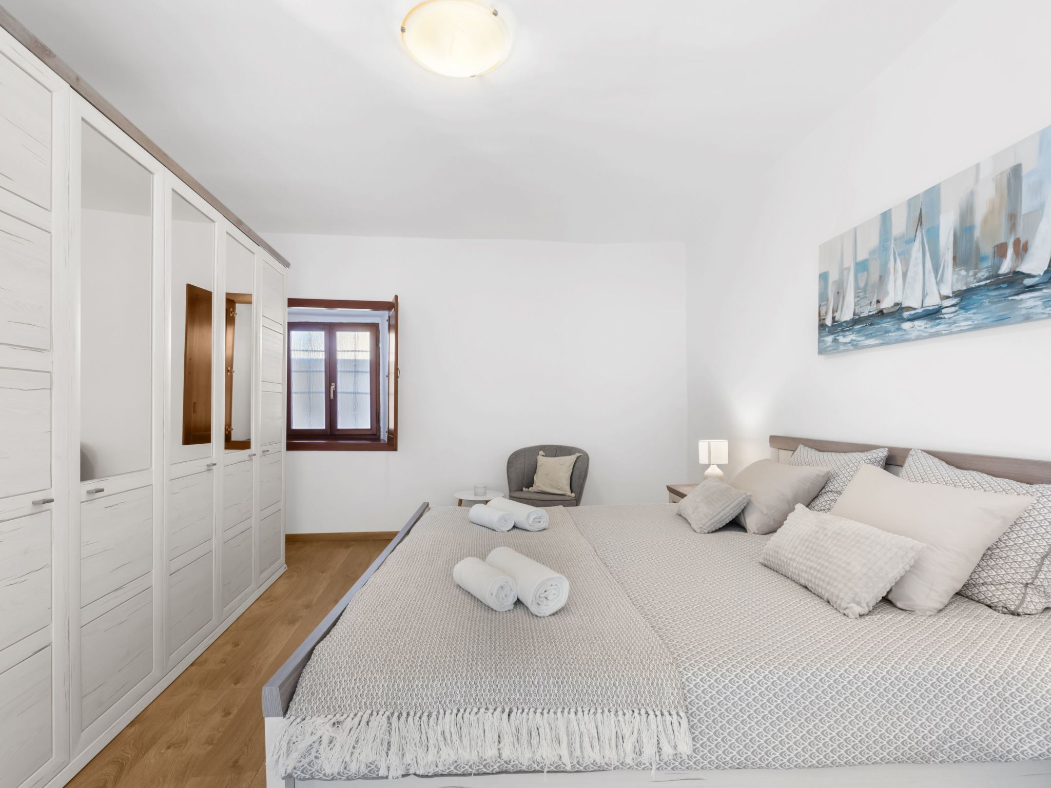 Een slaapkamer met een bed, een stoel, een nachtkastje, een kledingkast en een schilderij aan de muur.