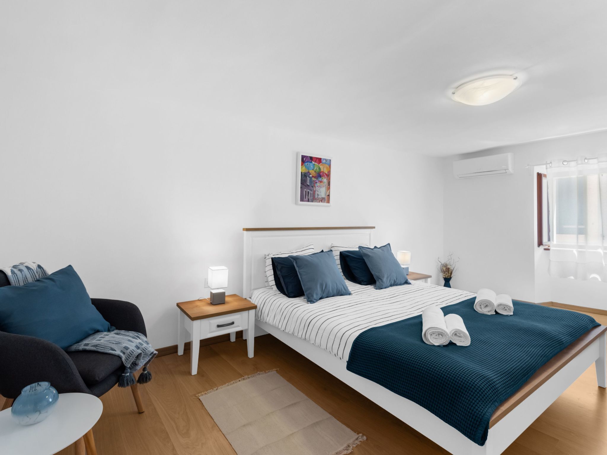 Ein modernes Schlafzimmer mit einem Bett, Nachttischen, einem Sessel und einem kleinen Tisch mit einer Vase.