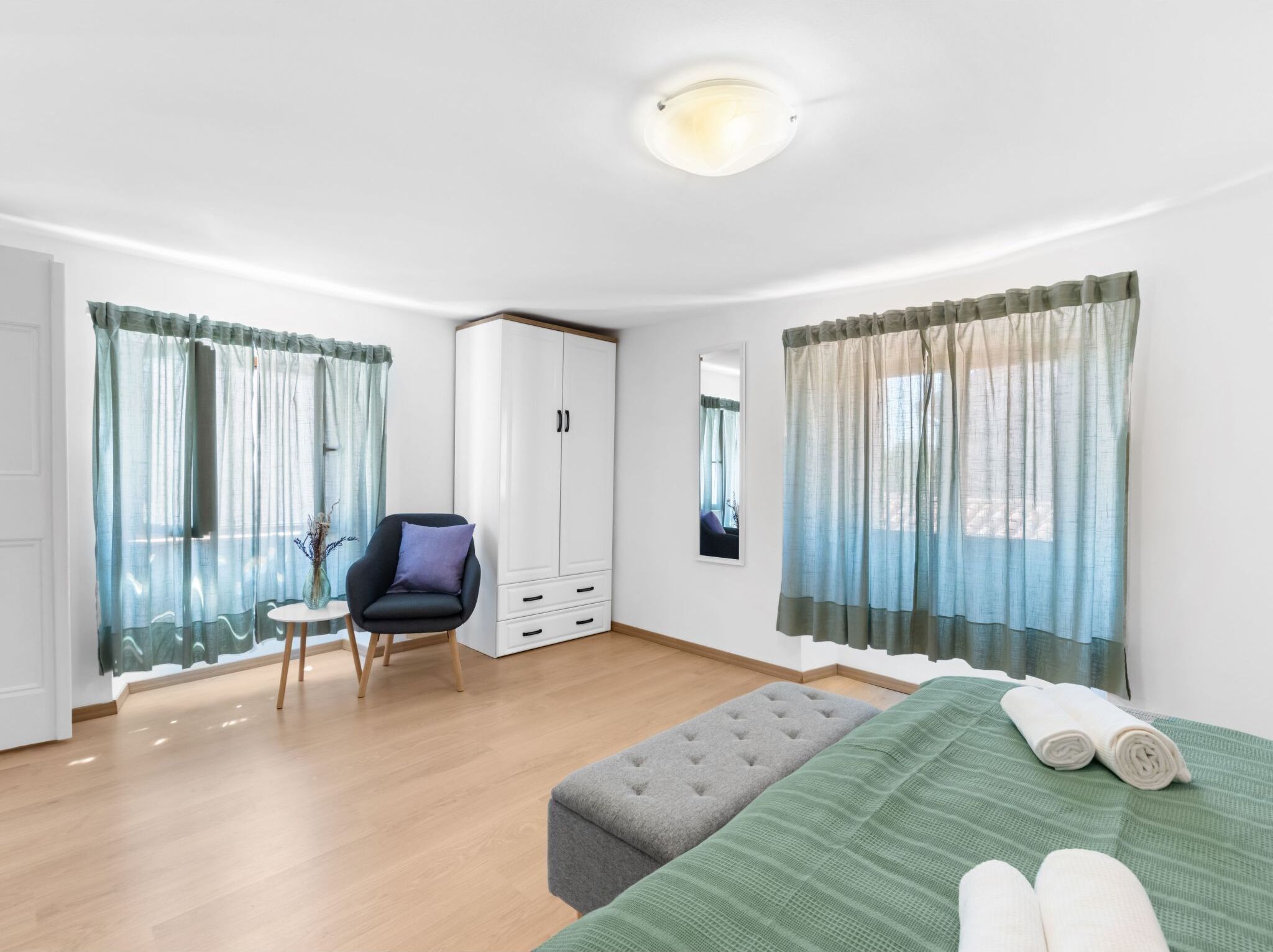 Un dormitorio moderno con cama, una silla, un armario y una ventana con cortinas.