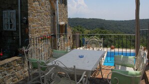Ein überdachter Außenbereich mit Tisch, Stühlen, einem Pool und einer Steinmauer.