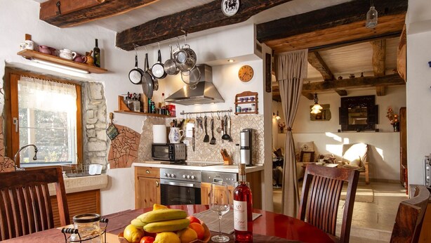 Eine gemütliche Küche mit Holzbalken, einer Steinwand und einer Essecke mit Tisch für zwei Personen.