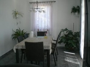 Un comedor con una mesa dispuesta para cuatro personas, rodeada de sillas. Hay plantas en macetas en las paredes y un candelabro sobre la mesa.
