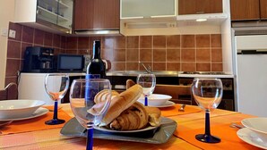 A dining area with a table set for two, featuring a bottle of wine, two wine glasses, a plate with croissants, and a bowl. - Apartment Santic by Interhome (Krk/Čižići)