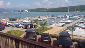 A marina with boats docked, a parking area with cars, and a view of the sea and hills in the background. - Insel Krk - Restauriertes  Steinhaus by Interhome (Krk/Čižići)