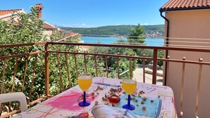 A balcony with a table set for two, overlooking a scenic view of a lake and hills. - Apartment Santic by Interhome (Krk/Čižići)
