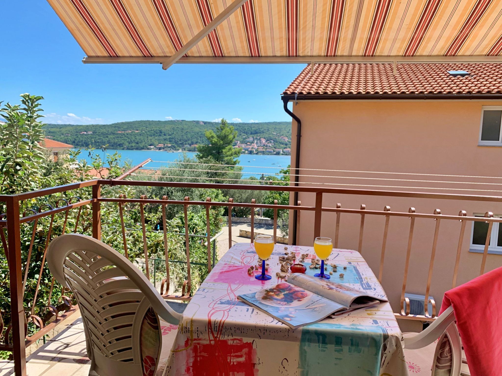 A balcony with a table set for two, overlooking a scenic view of a lake and hills.