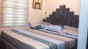 Una cama bien hecha con ropa de cama a rayas y almohadas, un cabecero gris y una ventana con persianas.