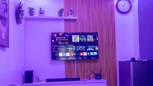 Una sala de estar con un televisor de pantalla plana montado en la pared, un mueble blanco debajo y un reloj en la pared.