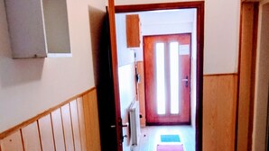 Un couloir aux murs lambrés, une porte au fond et une petite table sur laquelle repose un dépliant.