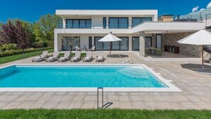 Une maison moderne à deux étages dotée d’une piscine, d’un espace salon extérieur et d’un patio.