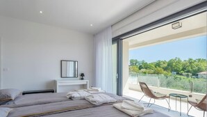 Une chambre d’hôtel moderne avec deux lits, une petite table de chevet, un miroir et un balcon donnant sur un paysage verdoyant.