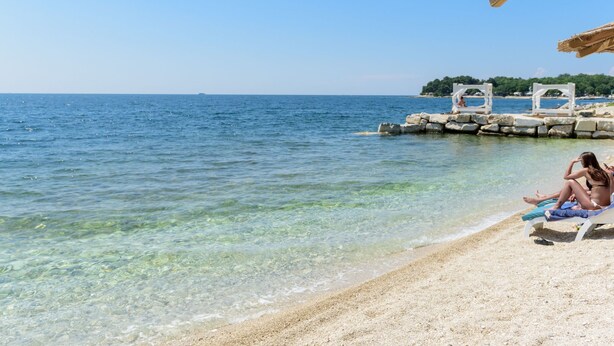 A beach with clear water, a thatched umbrella, and a lounge chair. - Villa Linet 3 by Interhome (Poreč/Funtana)