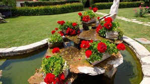 A garden with a stone fountain surrounded by red flowers and a well-maintained lawn. - Villa Linet 3 by Interhome (Poreč/Funtana)
