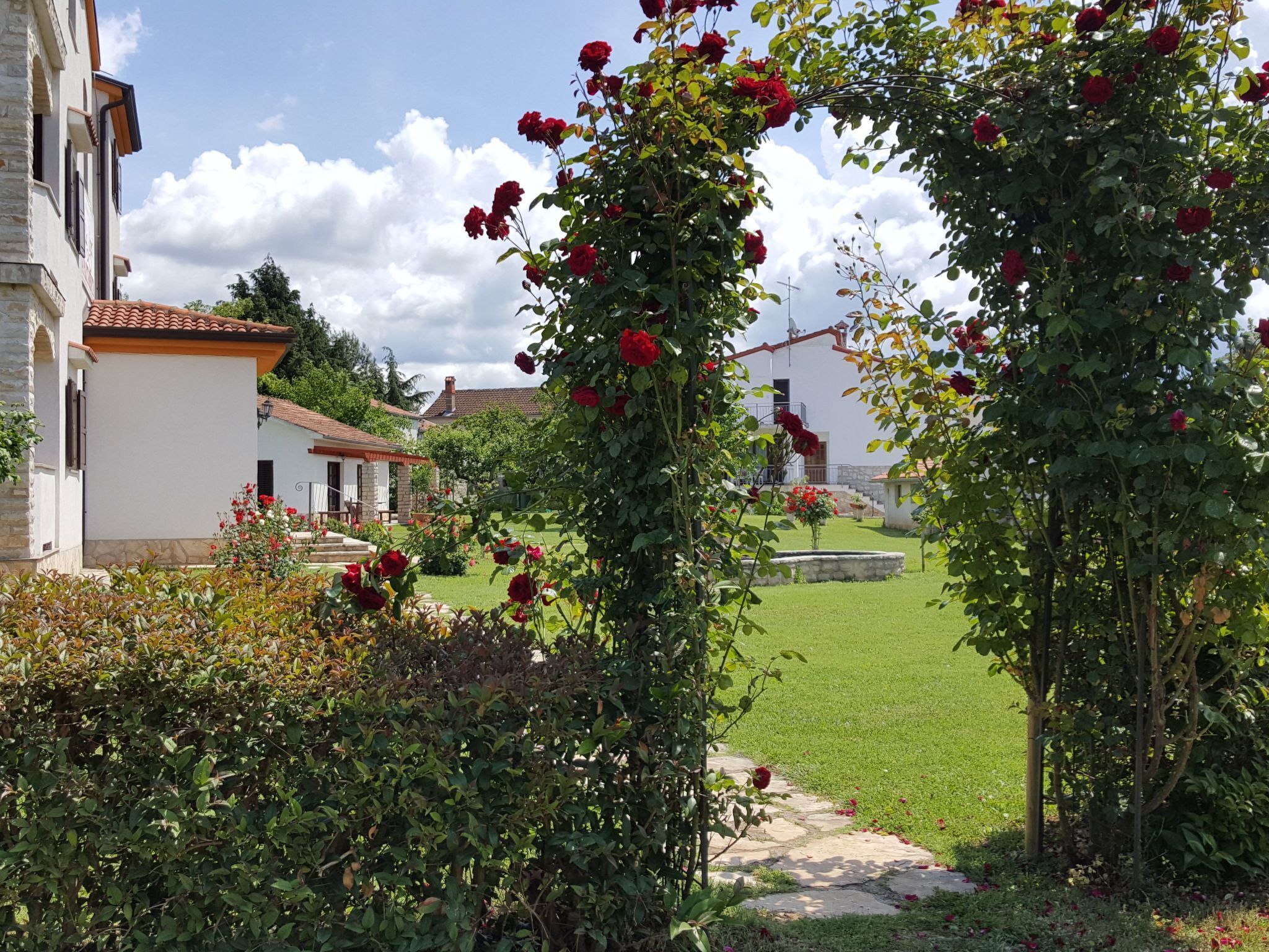 A garden with a rose archway leading to a white building with a tiled roof.