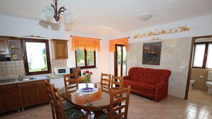 A dining area with a round table and chairs, a red sofa, and a kitchen with wooden cabinets and a microwave. - Villa Linet 3 by Interhome (Poreč/Funtana)