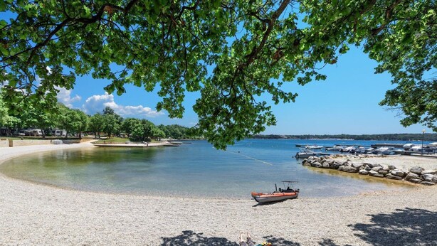 Una platja amb platja de pedres, un vaixell i una persona prenent el sol.