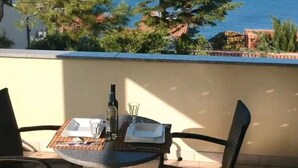Ein Balkon mit Tisch für zwei Personen, mit Blick auf die Küste, Bäume und das Meer.