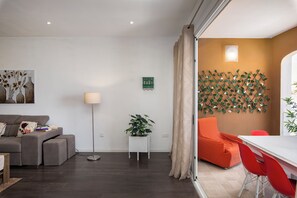A modern living room with a sofa, a small table, a floor lamp, and a dining area with a table and chairs. - Luxury 3BR APT with Terrace & Views (Zurrieq)