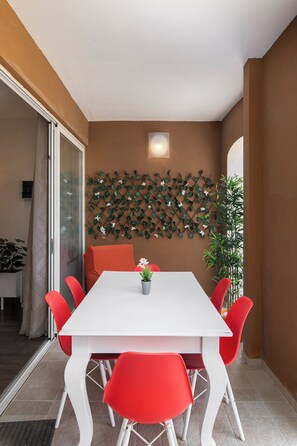 A dining area with a white table and red chairs, a decorative wall with a lattice pattern, and a potted plant. - Luxury 3BR APT with Terrace & Views (Zurrieq)