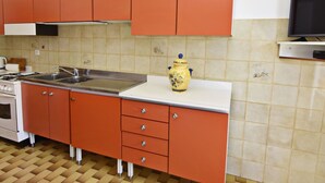 A kitchen with orange cabinets, a white countertop, a yellow vase, a stove, and a television. - Wohnung in der Nähe des Strandes Basanija by Interhome (Umag/Savudrija)