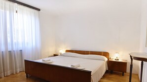 A neatly made bed with a wooden headboard, a bedside table with a lamp, and a small table with a lamp. - Wohnung in der Nähe des Strandes Basanija by Interhome (Umag/Savudrija)