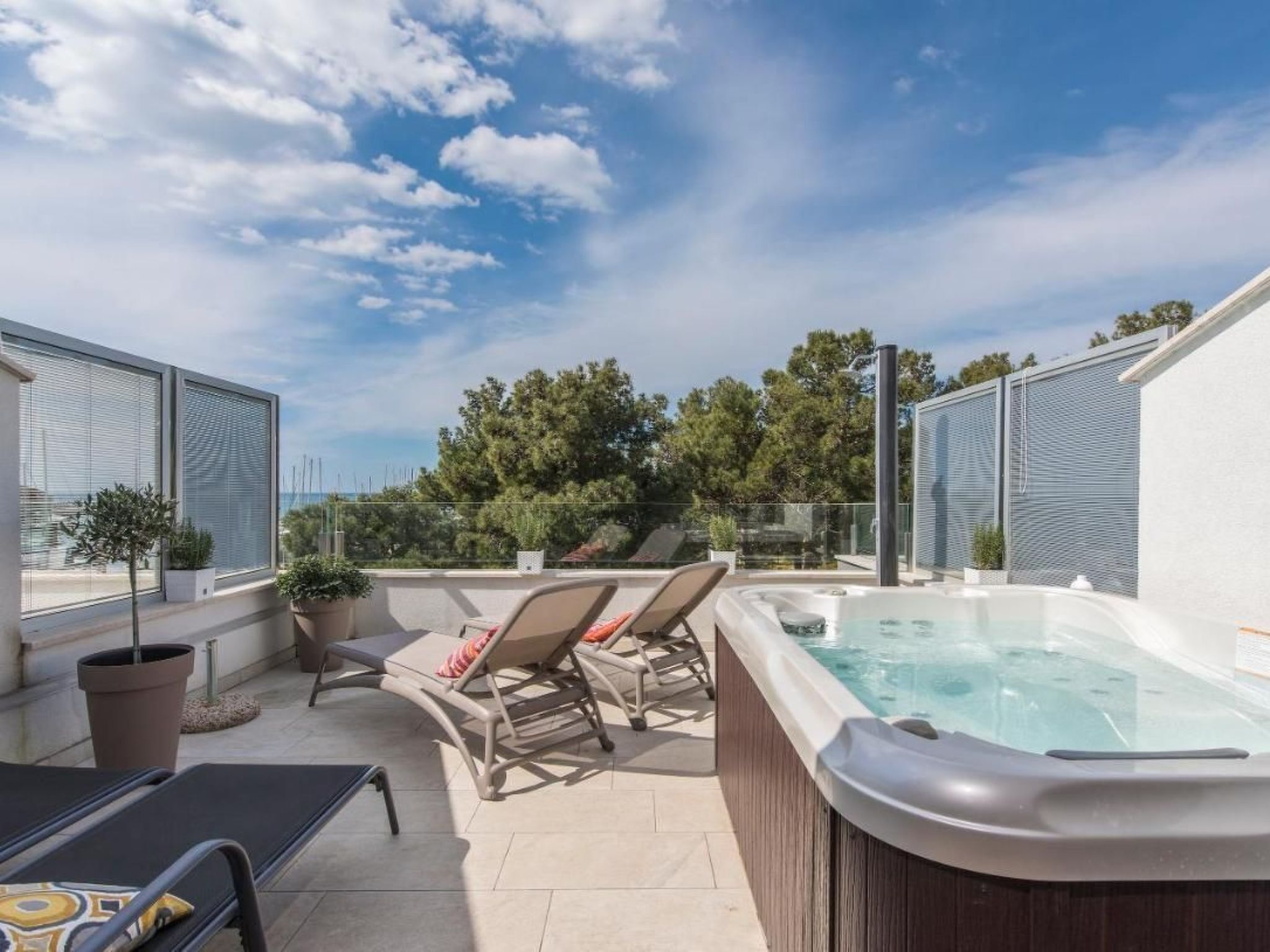 Een terras op het dak met een jacuzzi, lounge stoelen en plantenpotten.