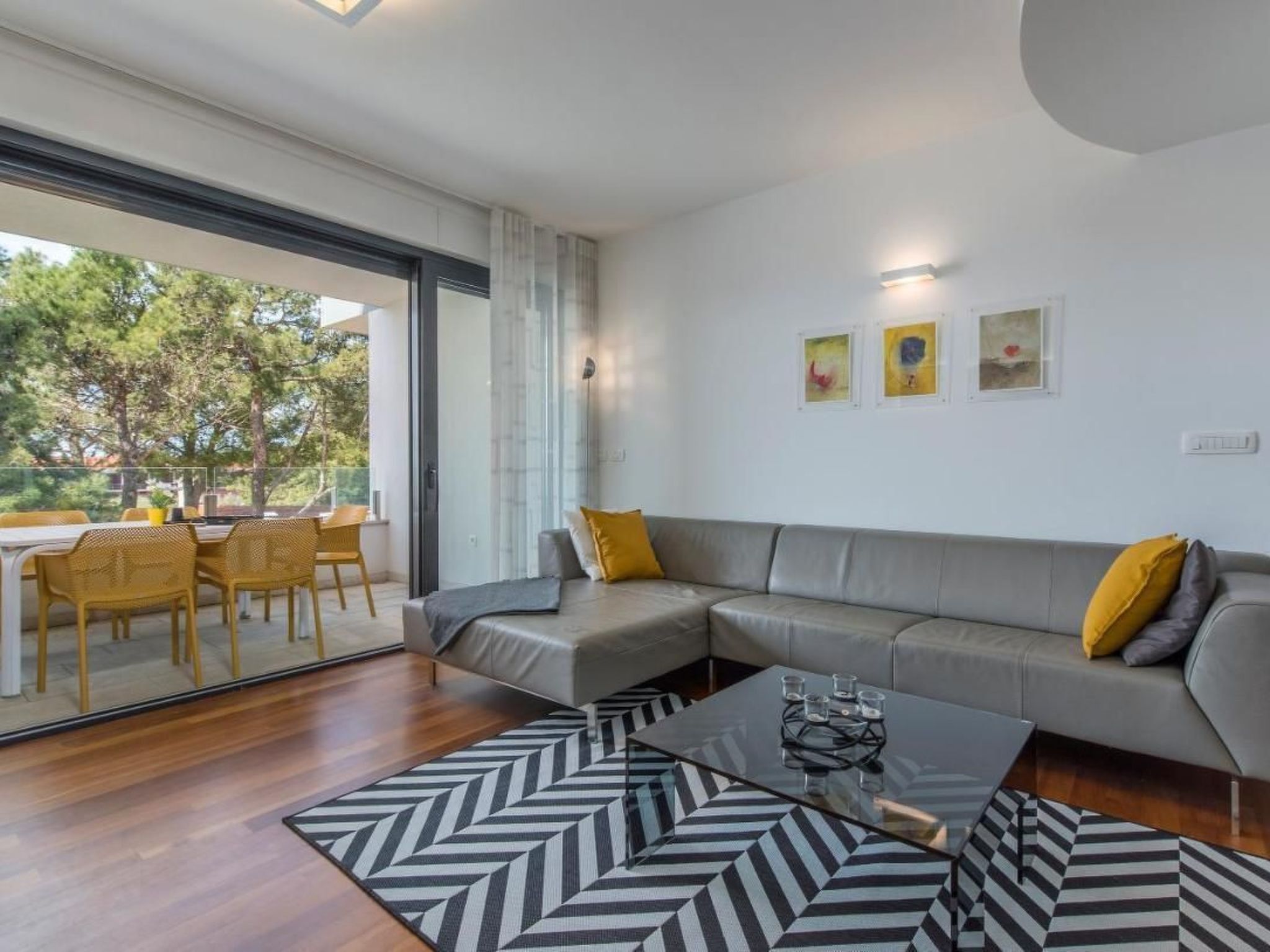 A modern living room with a grey sectional sofa, yellow cushions, a glass coffee table, and a patterned rug.