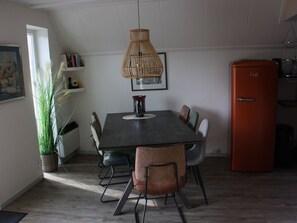 A dining area with a dark wooden table, six chairs, a woven pendant light, and a red refrigerator. - Haus Reiher am Lauwersmeer by Interhome (Anjum)