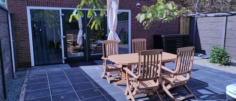 A patio with a wooden table and chairs, a glass door entrance, and a brick wall.