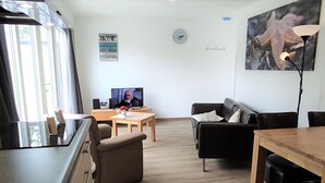 Ein Wohnzimmer mit Fernseher, Sofa und Esstisch.