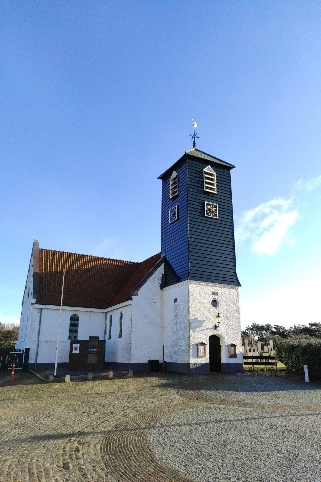 En kyrka med ett markant torn som har en klocka och en vindflöjel.