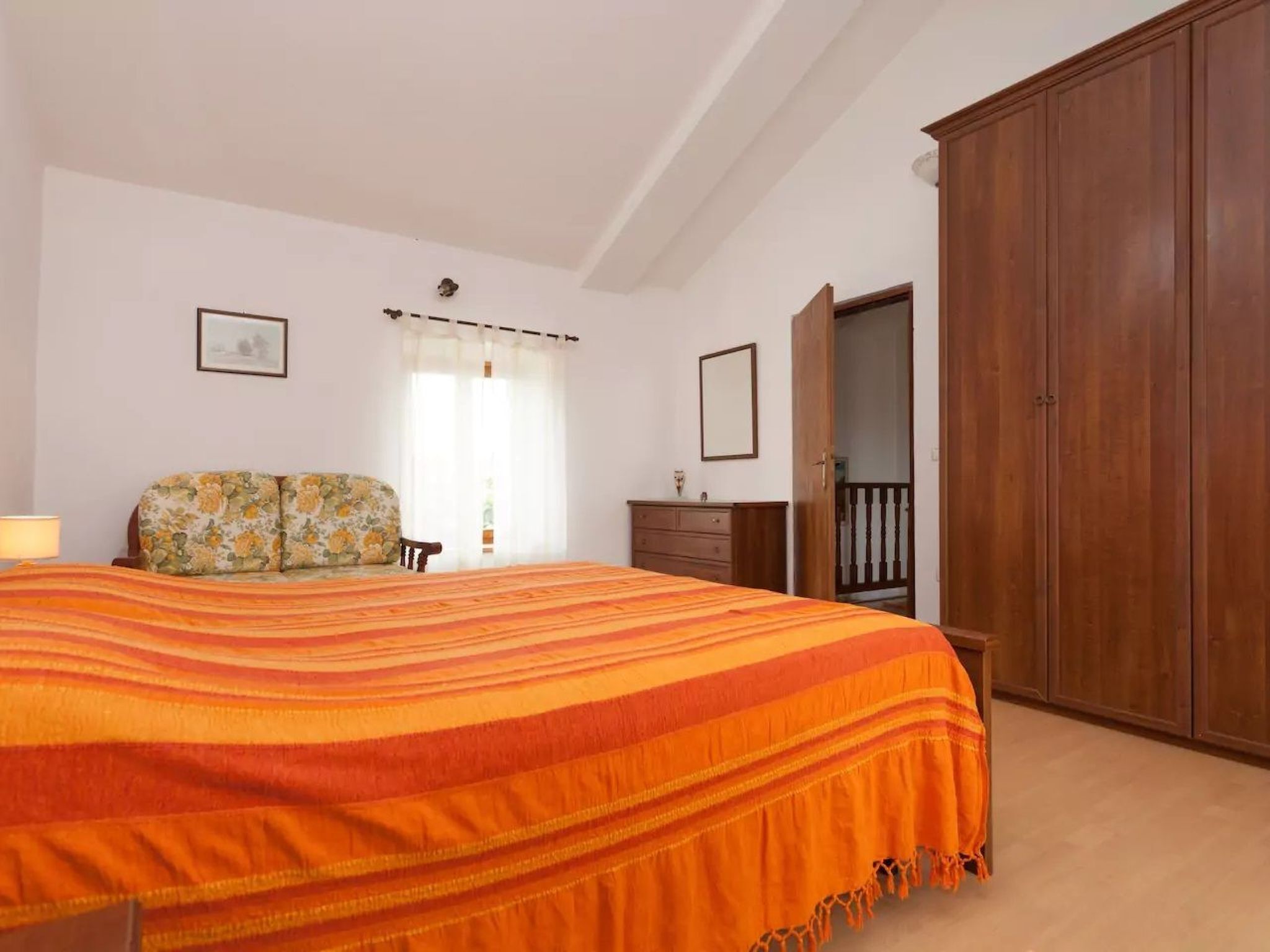 A bedroom with a large bed, a wooden wardrobe, a dresser, and a chair.