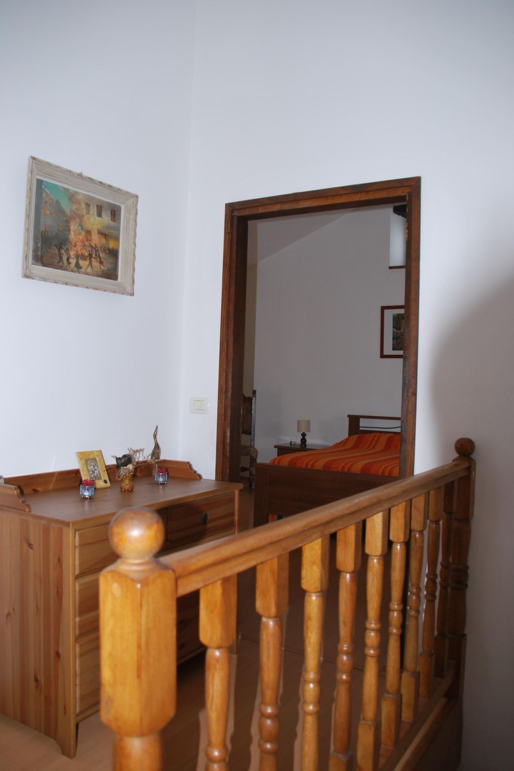 Een slaapkamer met een houten dressoir, een bed met een oranje deken, een houten balustrade en een grote spiegel die de kamer weerspiegelt.