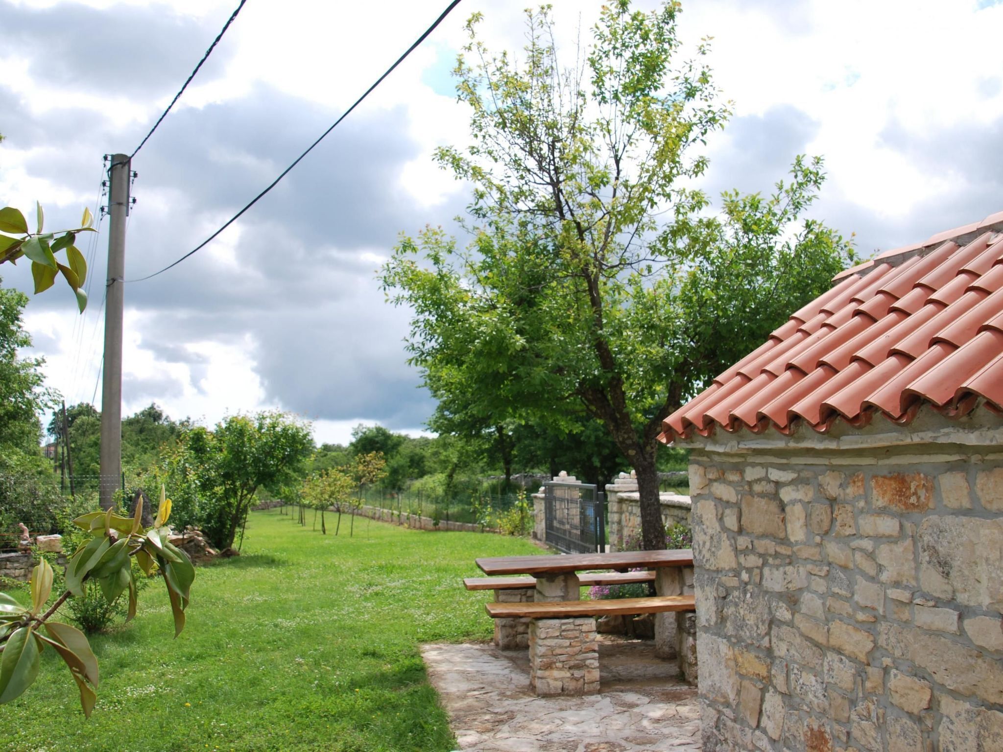 Un bâtiment en pierre avec un toit en tuiles, une table de pique-nique et une zone herbeuse avec des arbres.