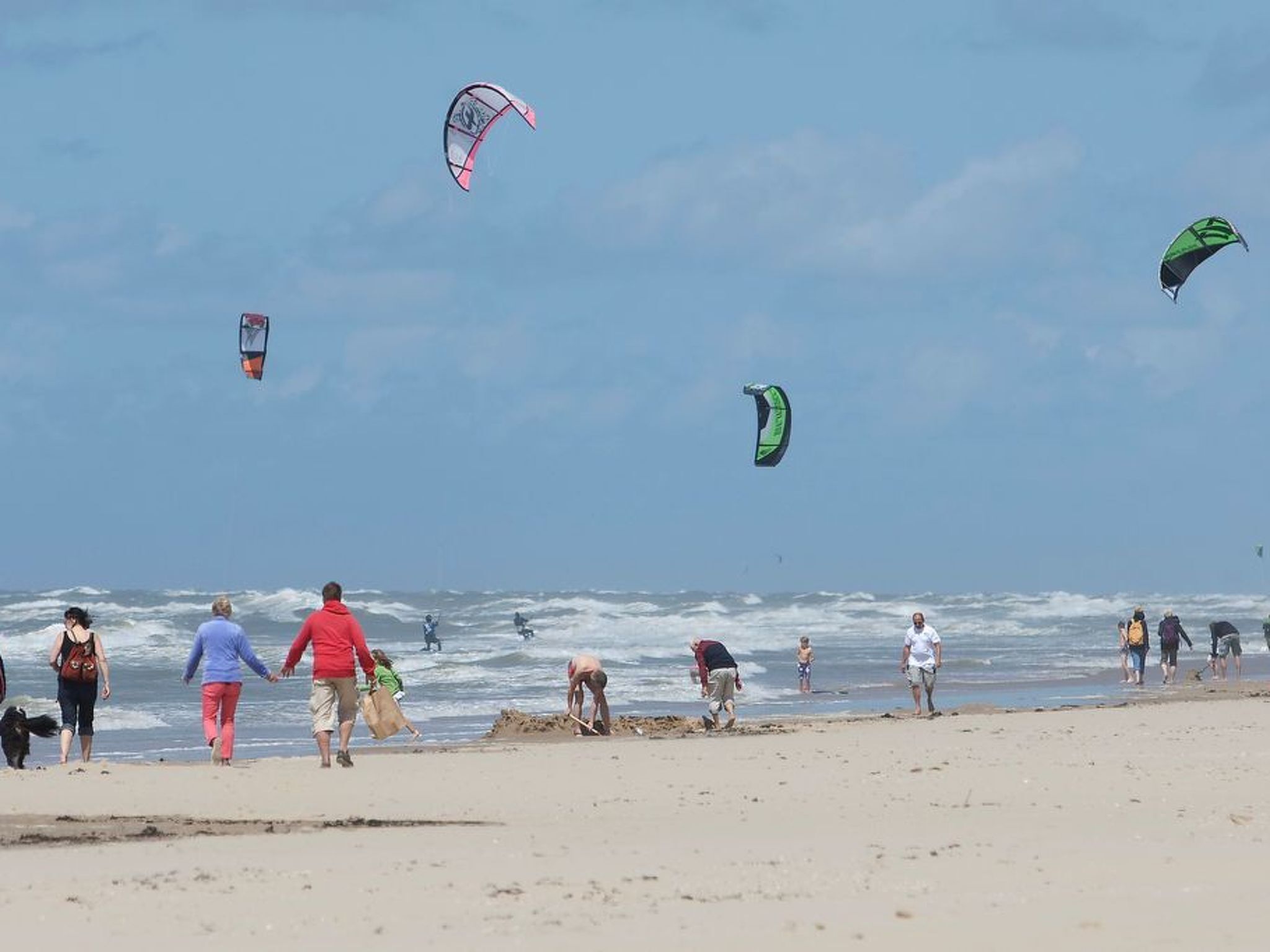Een strand met mensen die wandelen en vliegeren.