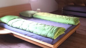 Un letto singolo con biancheria verde e blu in una stanza con pareti in legno e soffitto spiovente.