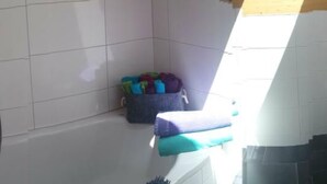 Angolo di una stanza con pareti in piastrelle bianche, soffitto in legno e un piccolo cesto contenente oggetti colorati.