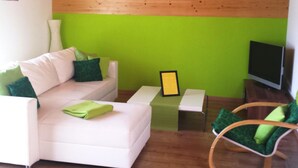 Un soggiorno con un divano bianco, cuscini verdi, un tavolino, una televisione e un soffitto in legno.