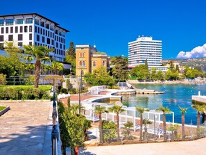 Een waterkantpromenade met moderne gebouwen, een jachthaven en palmbomen.