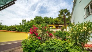 A courtyard with a paved walkway, lush green foliage, and a yellow building with a red roof. - mit Wasserblick by Interhome (Opatija)
