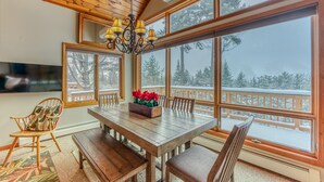 Ein Essbereich mit Holzboden, einem Tisch, Stühlen und einer Kristallleuchter. Große Fenster bieten Blick auf eine verschneite Terrasse.