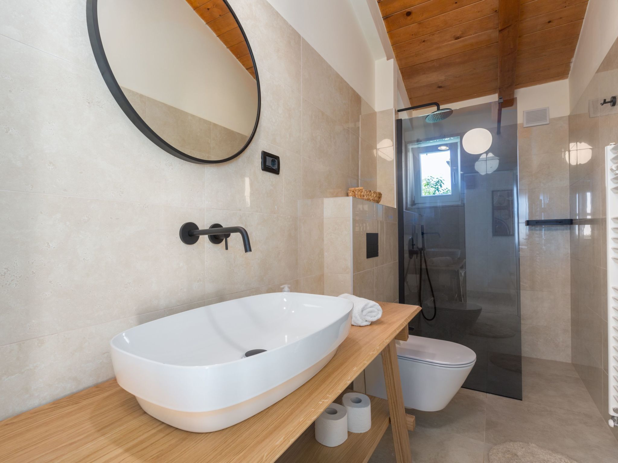 Un bagno moderno con un ampio lavandino ovale, uno specchio rotondo e una cabina doccia in vetro.