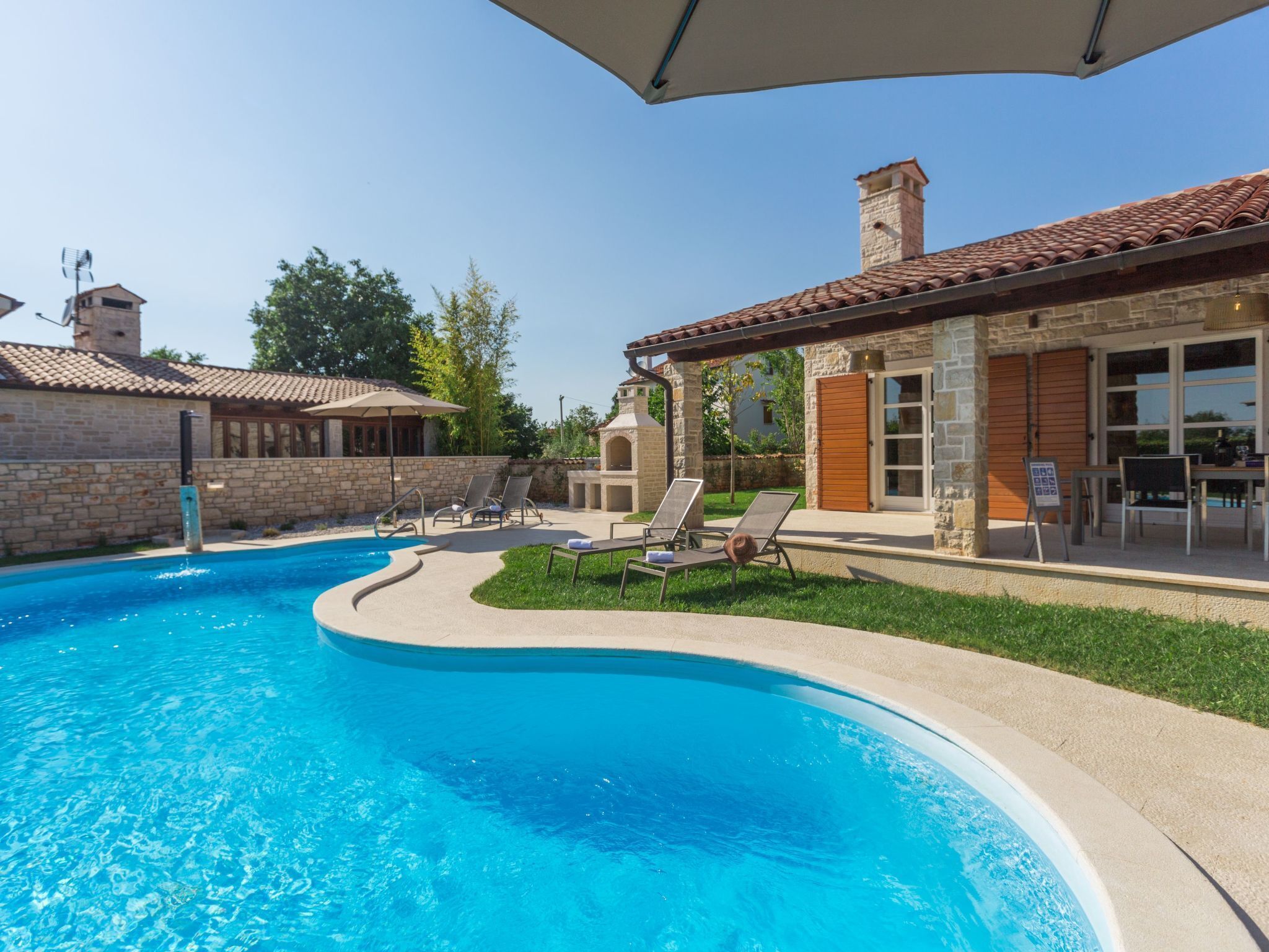 A swimming pool with lounge chairs and a stone building with a tiled roof.